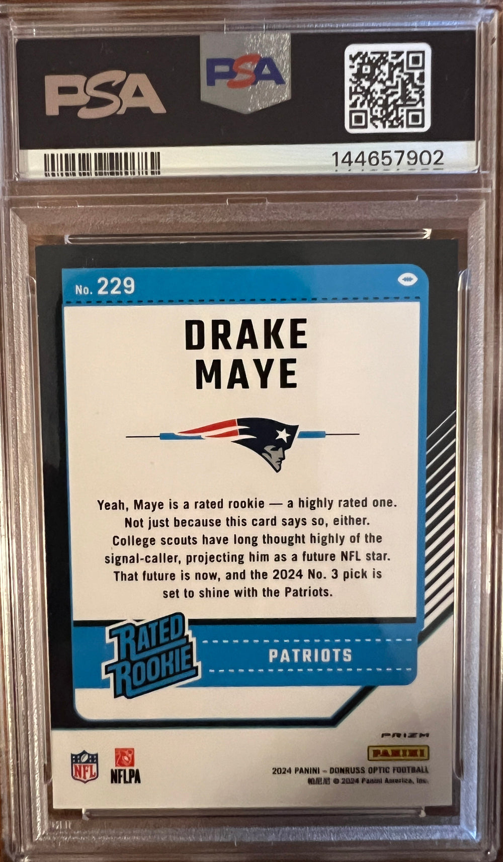 A graded 2024 Donruss Optic Drake Maye trading card, PSA 9 Mint Purple Shock, encapsulated in a clear plastic holder and placed on a dark wood background (back of card)