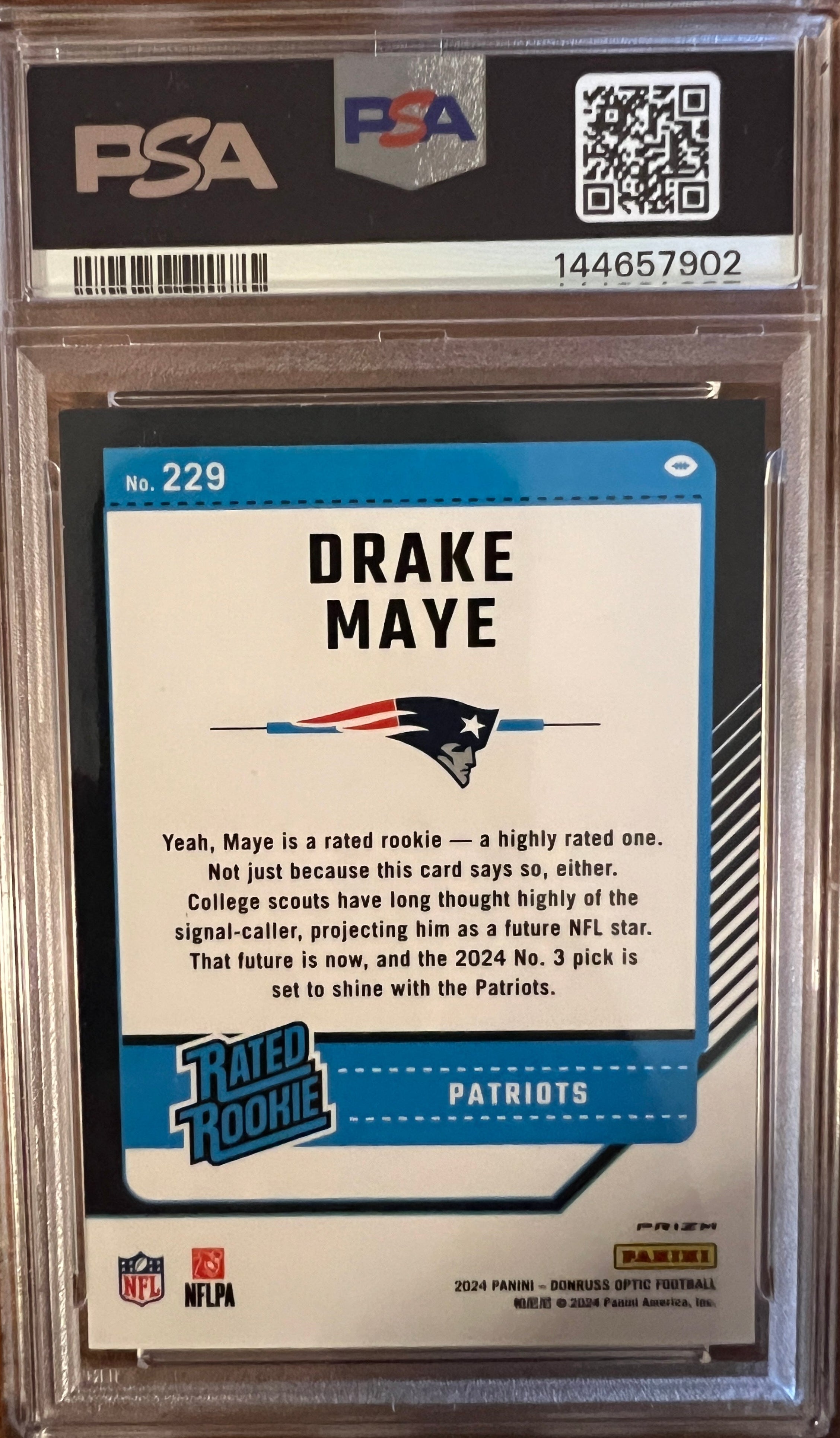 A graded 2024 Donruss Optic Drake Maye trading card, PSA 9 Mint Purple Shock, encapsulated in a clear plastic holder and placed on a dark wood background (back of card)